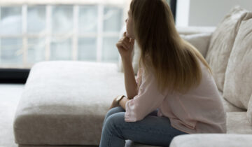 Lonely woman sitting on couch in living room, looking away